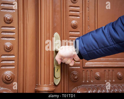 The man opens the closed old door. Old handle and hand in winter jacket. Stock Photo