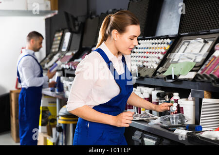 Smiling cheerful positive  female car painter preparing paints for paintwork in modern auto repair shop Stock Photo