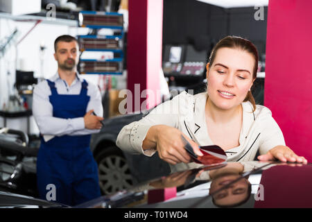 Smiling female client with paint samples choosing color for painting car at auto repair shop Stock Photo