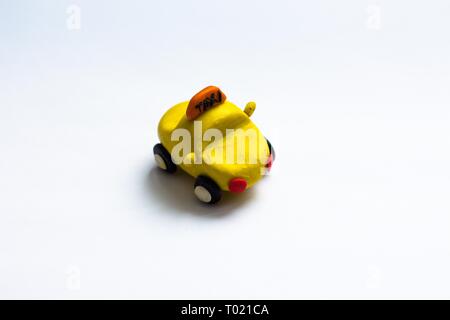 A small yellow cab made of plasticine stands on a white background. The car wheels are black and red headlights. Stock Photo