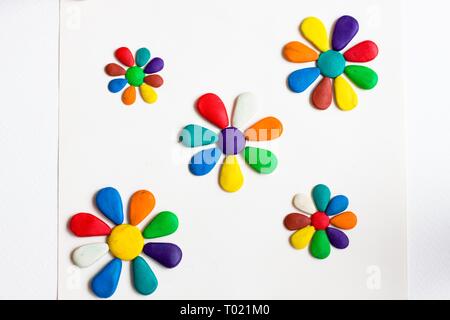 Several flowers with colorful petals of various colors lie on a white background. Flowers are made of plasticine. Stock Photo