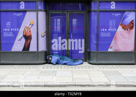 London, UK. 16th March, 2019. A man walks past a homeless man asleep on Piccadilly. Penelope Barritt/Alamy Live news Stock Photo