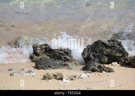 Ocean waves from a crystal clear beach slapping against around rocks Stock Photo