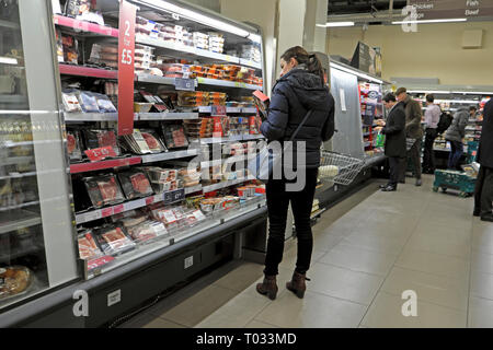 A woman shopper checking out the price of oven ready meal on a refrigeration food shelf in Marks & Spencer store in London England UK  KATHY DEWITT Stock Photo