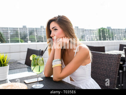 A beautiful girl is bored and sad, waiting for boyfriend or girlfriend. Waiting for phone call. Emotions of disorder, sadness. A woman in white dress Stock Photo