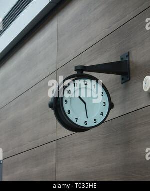 Round white clock with Roman numerals mounted side view on the wall of a public building Stock Photo