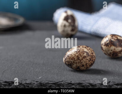 Three small eggs on a stone counter. A blue napkin and a metal tray in the background. Stock Photo
