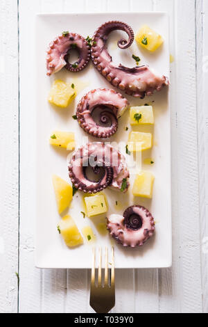 Octopus and potatoes salad with an elegant style,   pieces of boiled octopus and potatoes, over a rectangular elegant dish over a wooden background, t Stock Photo