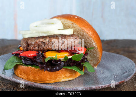 Venison burger in brioche bun with peppery leaf salad, onion and roast peppers Stock Photo