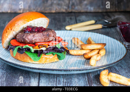 Venison burger in brioche bun with peppery leaf salad, onion, roast peppers and lingonberry sauce Stock Photo