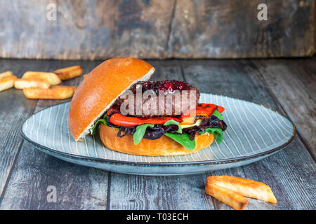 Venison burger in brioche bun with peppery leaf salad, onion, roast peppers and lingonberry sauce Stock Photo