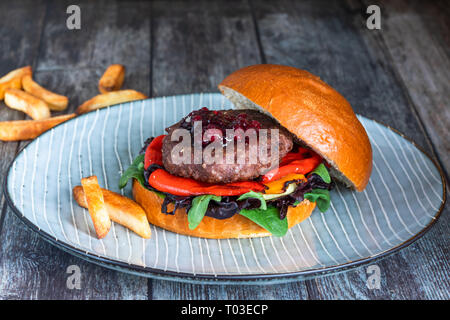 Venison burger in brioche bun with peppery leaf salad, onion, roast peppers and lingonberry sauce Stock Photo