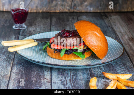 Venison burger in brioche bun with peppery leaf salad, onion, roast peppers and lingonberry sauce Stock Photo