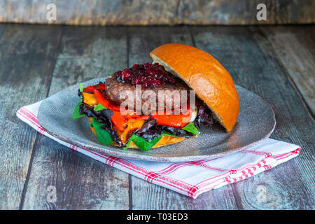 Venison burger in brioche bun with peppery leaf salad, onion, roast peppers and lingonberry sauce Stock Photo