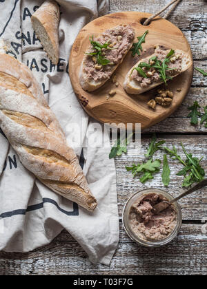 Two toasts with tender rillettes (pate) on white bread with arugula and walnut on a round wooden board on an old wooden background Stock Photo