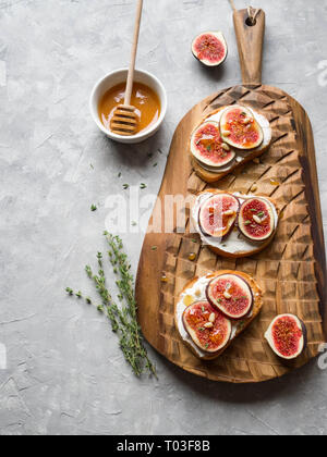 Three toasts with ricotta and figs with honey thyme and pine nuts on a board on a gray background Stock Photo