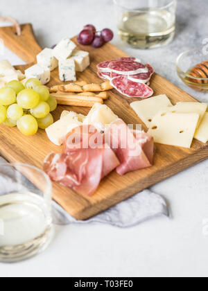 Cheese and meat wine snack set on wood board . Variety of cheese, salami, prosciutto, bread sticks, honey, grapes and two glasses with wine. Stock Photo