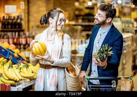 Young and happy couple buying food, choosing fresh fruits in the supermarket