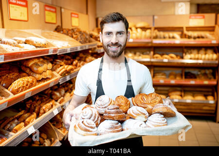 Portrait of a handsome baker in uniform standing with fresh pastries in the bakery deparment of the supermarket Stock Photo