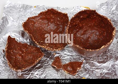 Broken chocolate Easter egg with chopped hazelnuts on a foil sheet against, UK. Stock Photo