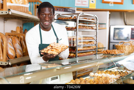 Successful baker working behind counter in bakeshop, presenting fresh baked products Stock Photo