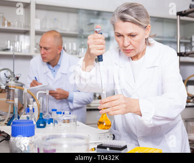 Scientific researching in laboratory. Focused mature female scientist injecting reagent into solution in test tube Stock Photo