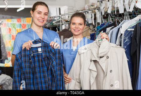 Young women workers of laundry holding clean garment, demonstrating quality of dry cleaning Stock Photo