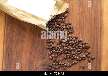 coffee bag lie on wodden table with spild coffee beans around product label cutout Stock Photo