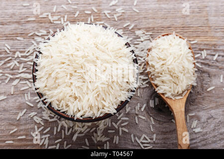 Uncooked rice in a wooden spoon and a clay plate. Dietary nutrition. Stock Photo