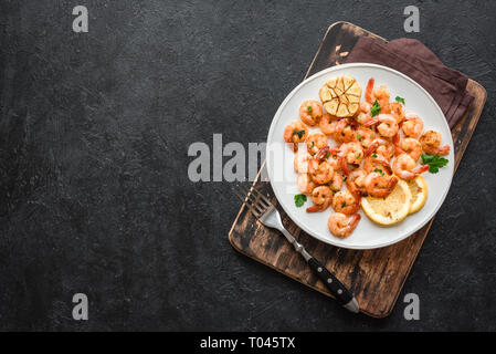 Roasted shrimps with lemon, garlic and herbs. Seafood, shelfish. Shrimps Prawns sauteed with spices, garlic and lemon on black stone background, copy  Stock Photo