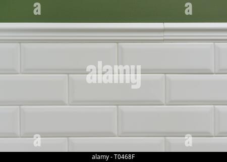 Green painted wall, part of the wall is covered tiles small white glossy brick, ceramic decorative molding tiles. Fragment of the walls of the bathroo Stock Photo