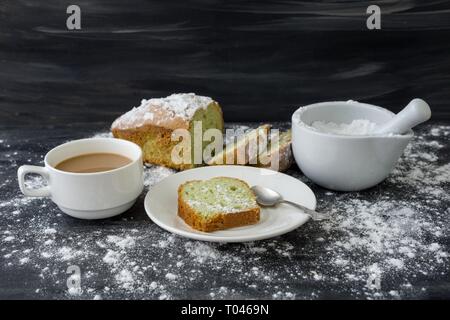 Mint cake sprinkled with powdered sugar on dark surface with cup of coffee. Stock Photo