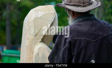 The man in black hat carving a big wood into an image using a machine to carve the big white wood into a big statue Stock Photo