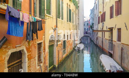 The small canal in the city of Venice surrounding with buildings and houses and the clothes hanging outside in Italy Stock Photo