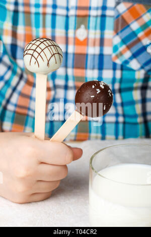 Two cake pops decorated with white and dark chocolate in children's hands. Dessert for small gourmets. Selective focus Stock Photo
