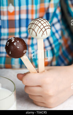 Two cake pops decorated with white and dark chocolate in children's hands. Dessert for small gourmets. Selective focus Stock Photo