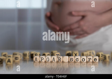Words APGAR SCORE composed of wooden letters. Pregnant woman in the background Stock Photo