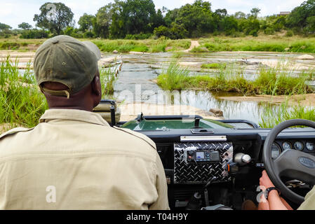Black man tracker sitting in safari Land Rover Defender safari vehicle crossing river in African bush, Sabi Sands game reserve, South Africa Stock Photo