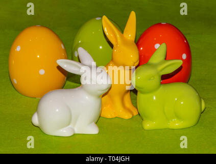 Colorful ceramic easter eggs and Easter bunnies in front of a green background. Stock Photo