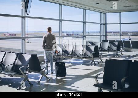 Traveler in airport terminal. Young man with luggage waiting for airplane. Stock Photo