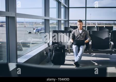 Traveler using laptop in airport terminal. Young man waiting for airplane. Stock Photo
