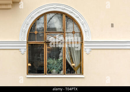 Triple arched window with a wooden frame and white stucco on the background of the wall of light beige. Stock Photo