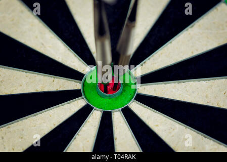 three darts thrown at the bulls eye of a dartboard Stock Photo
