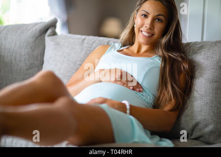 Positive pregnant woman in dress lying on the sofa home Stock Photo