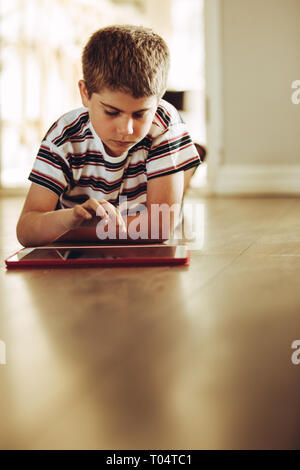 Boy sitting on floor at home using a tablet pc. Close up of a kid learning on a tablet computer. Stock Photo