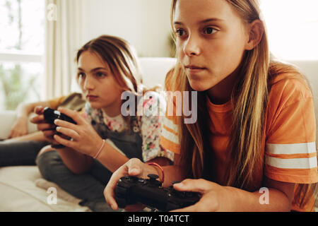 Close up of two teenage girls playing video game holding joysticks. Girls sitting on couch at home and playing video game with great interest.
