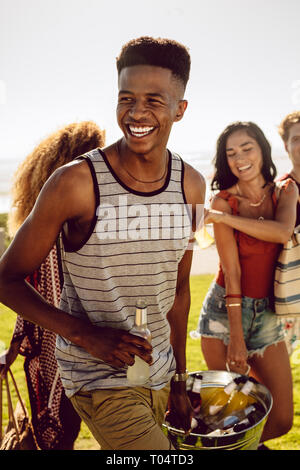 Young african man with friends going on picnic on summer day. Group of multi-ethnic friends having beers while walking to the picnic spot. Stock Photo