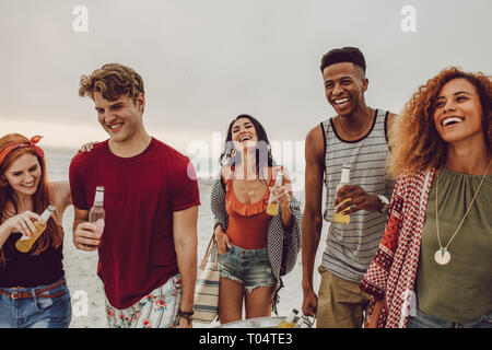 Group of people carrying beverage tub for party on beach. Diverse group of young people walking outdoors and having drinks. Stock Photo