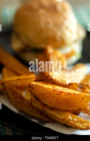 Plate of tasty hand cut fried to perfection chips fries with beef burger in bread bun. Stock Photo