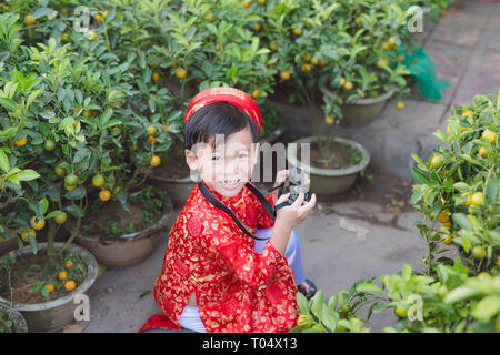 Child with digital compact camera outdoors. Cute little Vietnamese boy in ao dai dress smiling. Tet holiday Stock Photo